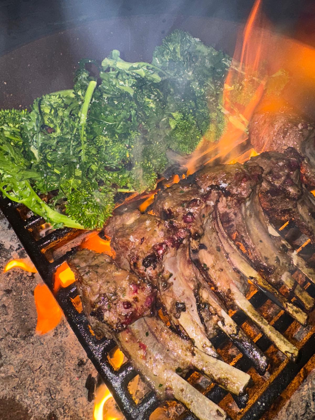 Lamb chops and broccolini cooking over open flame.
